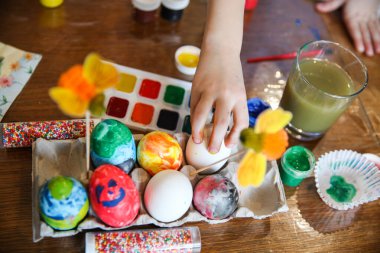 Çocuk Paskalya dekorasyonu için masanın üstündeki el işi tezgahından bir yumurta alıyor. Çerçevede sadece el var. Yüksek kalite fotoğraf