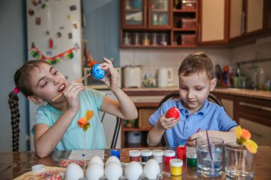 Esmer erkek ve kız kardeş evdeki masada oturan Paskalya yumurtalarını süslerler. Yüksek kalite fotoğraf
