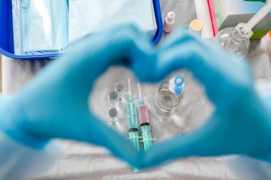 Mavi eldivenli bir hemşire kalp şeklindeki ellerini şırınga ve şişelerin üzerinde masanın üzerinde tutuyor. Üst Manzara. Coronavirus konsepti