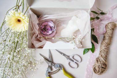 Beyaz bir masada beyaz bir hediye kutusunda pembe dekoratif mum. Çiçekçinin aletleri ve çiçekleri yakınlarda. Yüksek kalite fotoğraf