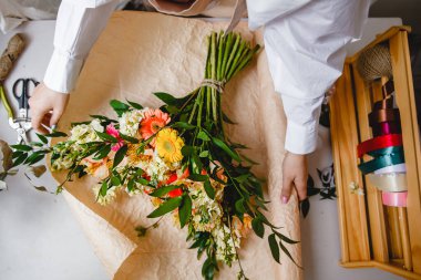 Beyaz gömlekli kadın bir çiçekçi bir buket taze çiçeği kağıda sarar. Üst Manzara. Yüksek kalite fotoğraf
