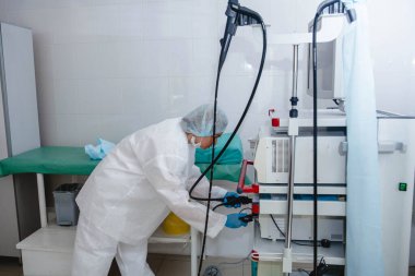 Beyaz koruyucu giysili, şapkalı ve eldivenli genç bir kadın endoskopist ekipmanları iş için hazırlıyor..