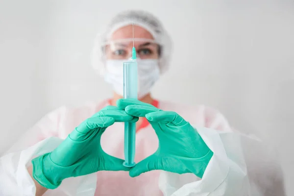 Un trabajador médico con una bata blanca, gorra blanca y guantes verdes sostiene una jeringa con una vacuna. Concepto de Coronavirus — Foto de Stock
