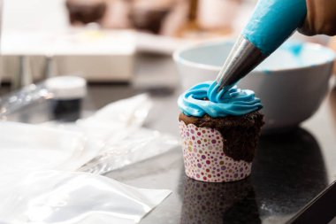 Dağınık mutfakta çikolatalı kek yapmak için mavi krema ekleyen bir kadın.