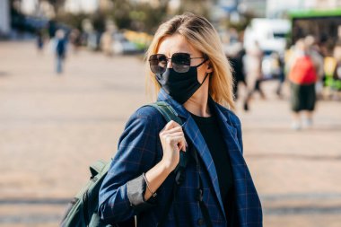 Kendini şehirde yürüyen koronavirüsten korumak için yüz kirliliği maskesi takmış yakışıklı bir kadın. 