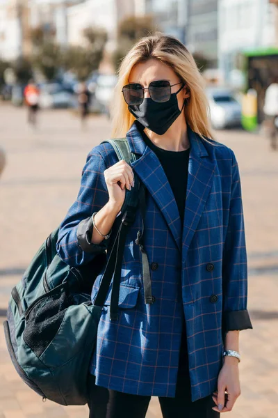 Young handsome fashion woman with backpack in face pollution mask to protect himself from the coronavirus walking in city