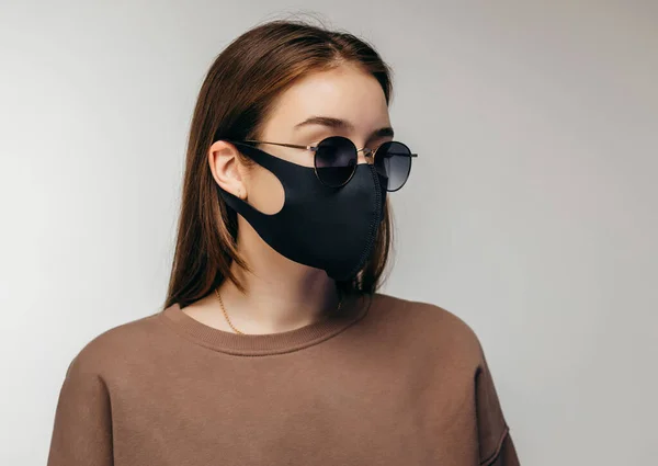 黒い顔のマスクとサングラスを身に着けている若い女性のスタジオの肖像画 クローズアップ 灰色の背景に隔離された — ストック写真