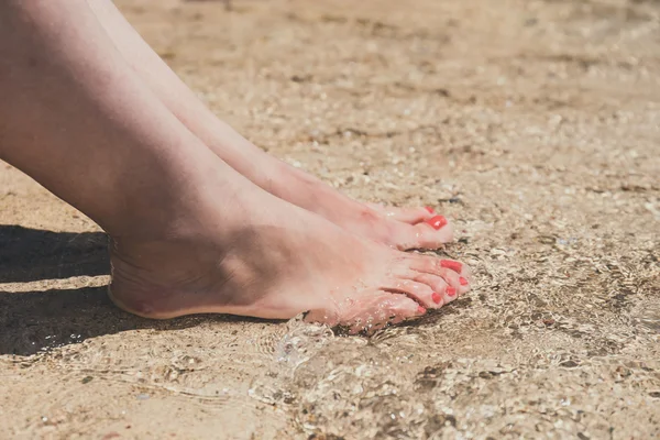 Female feet with red pedicure in beach sand, close up — Stock Photo, Image
