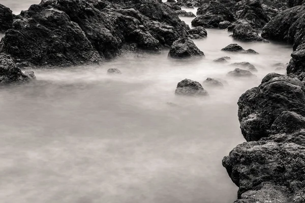 Движение размывает воду вокруг камней, черно-белая — стоковое фото