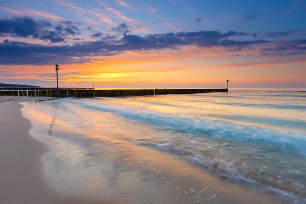 Pôr do sol na praia com um quebra-mar de madeira, longa exposição — Fotografia de Stock