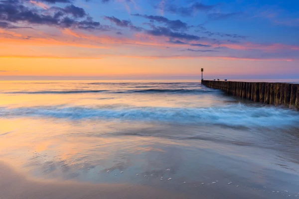 Solnedgång på stranden med en trä vågbrytare, lång exponering — Stockfoto