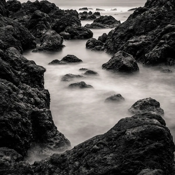 Movimiento borroso agua que rodea las rocas, blanco y negro — Foto de Stock