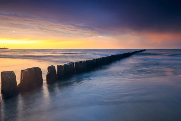 Sunset on the beach with a wooden breakwater, long exposure — Stock Photo, Image