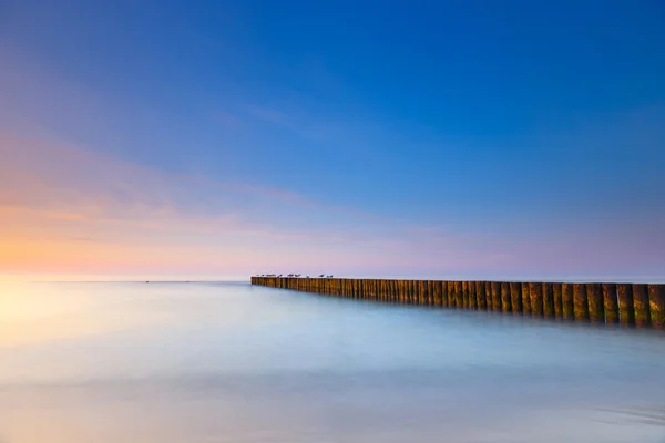 Ahşap bir dalgakıran, uzun pozlama ile sahilde günbatımı — Stok fotoğraf