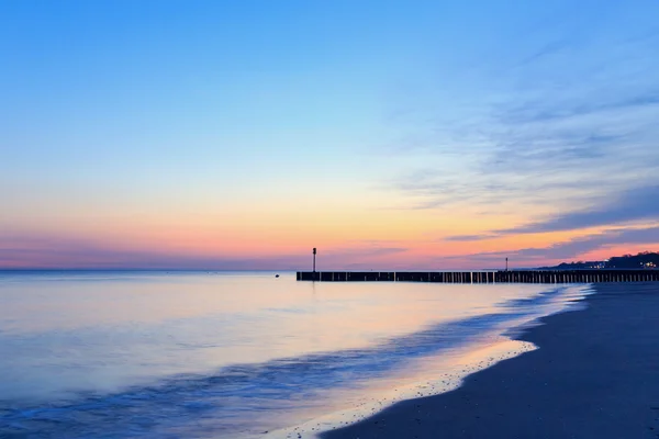 Zonsondergang op het strand met een houten golfbreker, lange blootstelling — Stockfoto