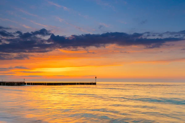 Puesta de sol en la playa con un rompeolas de madera, larga exposición — Foto de Stock