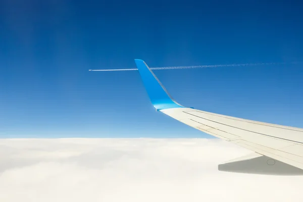 Крыло самолета, летящего над облаками на голубом фоне неба — стоковое фото