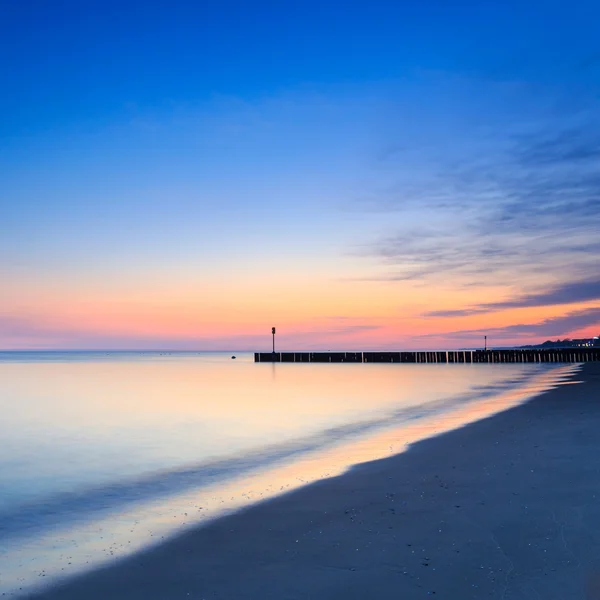 Sunset on the beach with a wooden breakwater, long exposure — Stock Photo, Image