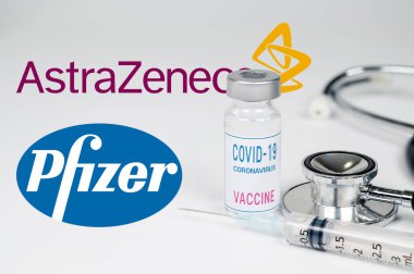 Seul, Güney Kore-Aralık 2020: COVID-19 Aşı Konsepti. Beyaz arka planda şırınga ve şişe. Arka planda AstraZeneca ve Pfizer şirket logosu var..