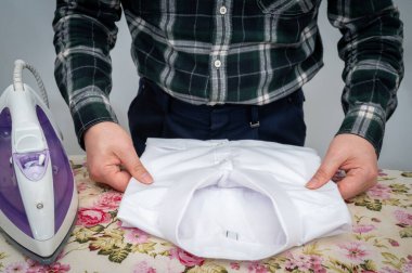 Ütü masasında giysileri ütüleyen bir adam..