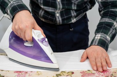 Ütü masasında giysileri ütüleyen bir adam..