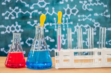 Tahta arka planı ve çeşitli kimyasal formülleri olan laboratuvar camları..