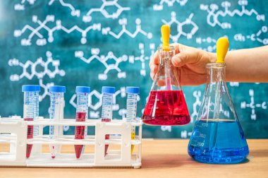 Tahta arka planı ve çeşitli kimyasal formülleri olan laboratuvar camları..