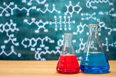 Tahta arka planı ve çeşitli kimyasal formülleri olan laboratuvar camları..