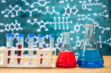 Tahta arka planı ve çeşitli kimyasal formülleri olan laboratuvar camları..