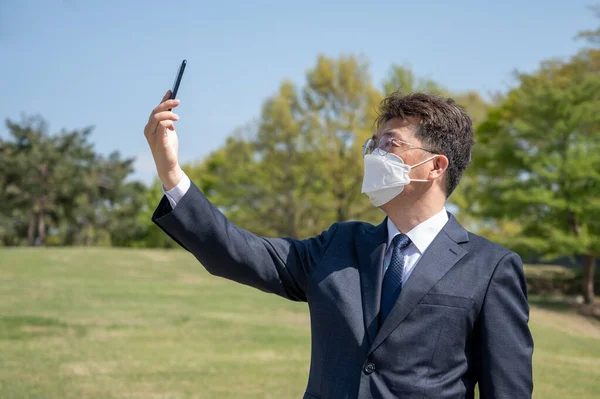 Midaldrende Asiatisk Forretningsmand Iført Maske Ved Hjælp Smartphone Græsplænen - Stock-foto
