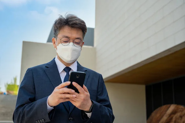 Midaldrende Asiatisk Forretningsmand Byen Iført Maske Ved Hjælp Smartphone - Stock-foto