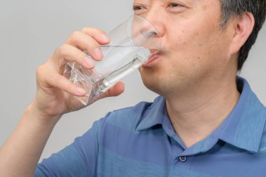 Orta yaşlı Asyalı bir adam elinde bir bardak su tutuyor..