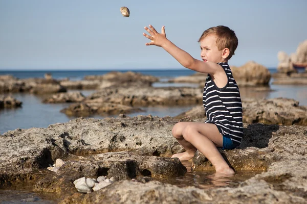 Liten pojke kastar stenar i havet — Stockfoto