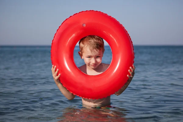 Liten pojke utseende av uppblåsbar ring i havet — Stockfoto