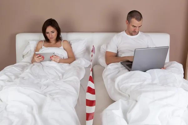 Casal jovem usando tablet e computador na cama . — Fotografia de Stock