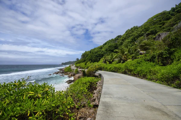 Odlivu na divoké východního pobřeží La Digue, Seychely s jedinou silnici v popředí — Stock fotografie