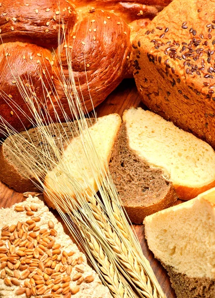 Pão fresco, espigas de trigo, grãos de trigo no fundo de madeira — Fotografia de Stock