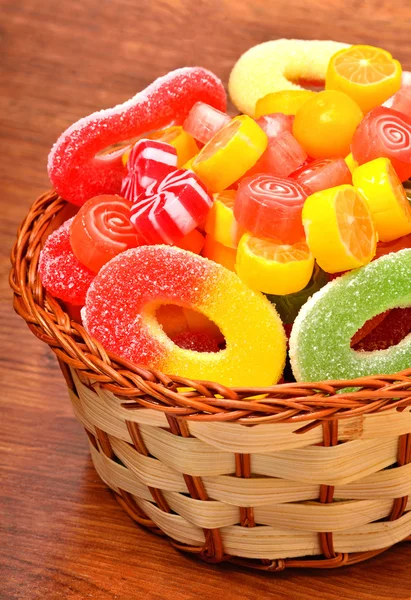 Dulces brillantes, piruletas, jaleas en la canasta de mimbre sobre el fondo de madera — Foto de Stock