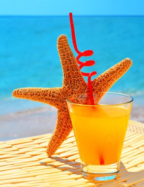 Fishstar, glass of orange cocktail against the blue sea clipart
