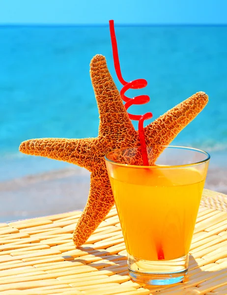 Fishstar, glass of orange cocktail against the blue sea — Stock Photo, Image