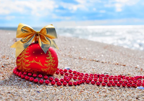 Boule de Noël rouge avec noeud doré sur le sable — Photo