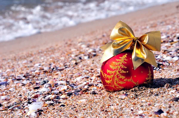 Boule de Noël rouge avec noeud doré sur le sable — Photo