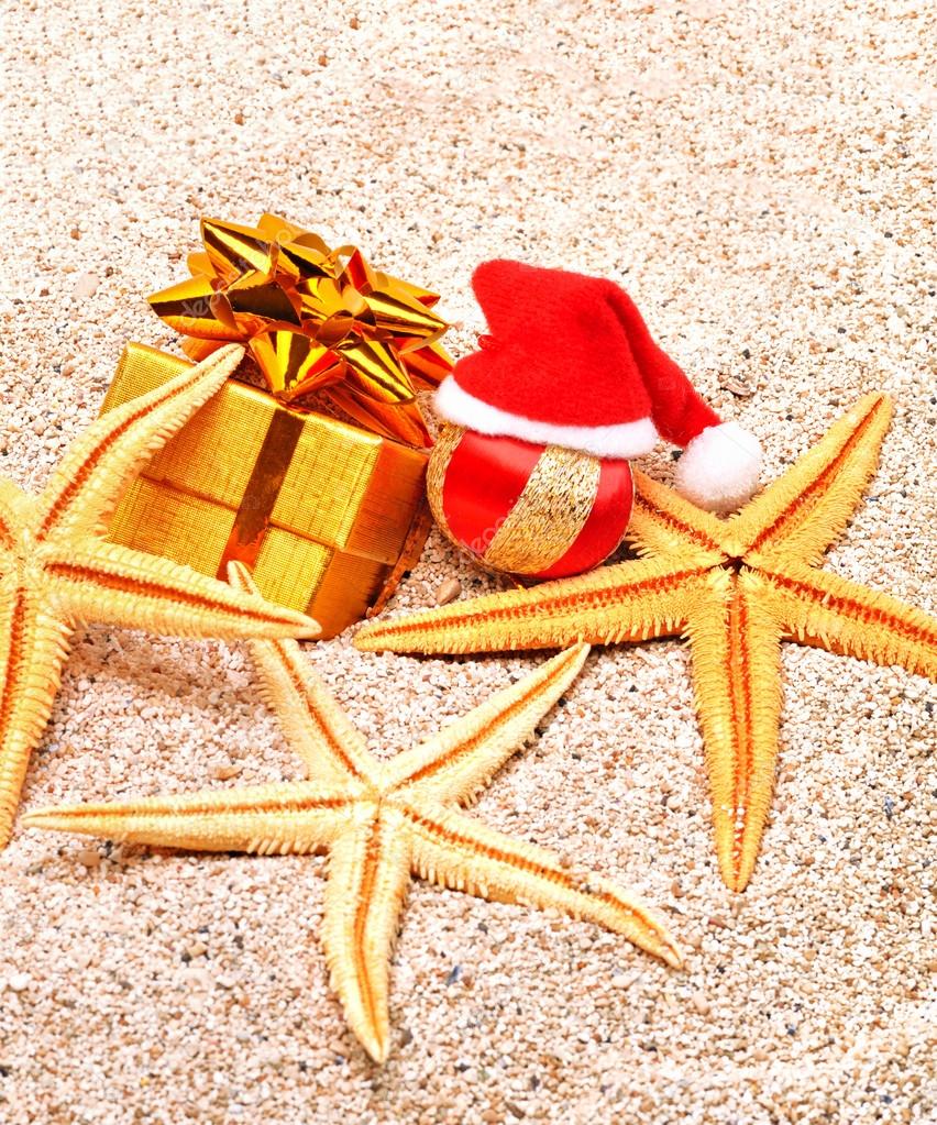 christmas bauble, starfishes and a gift box on  sand