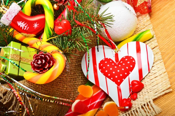 Christmas pine twigs, heart, christmas balls with pine cones, sweets and jellies on sacking background — Stock Photo, Image