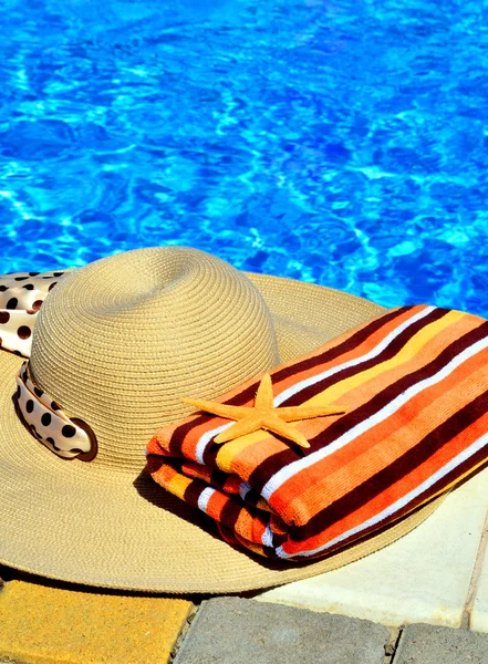 Woman beach hat, bright towel against blue swimming pool — Stock fotografie