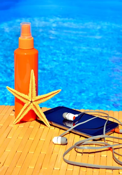 Cell phone, sun spray, head phones and starfish near water — Stok fotoğraf