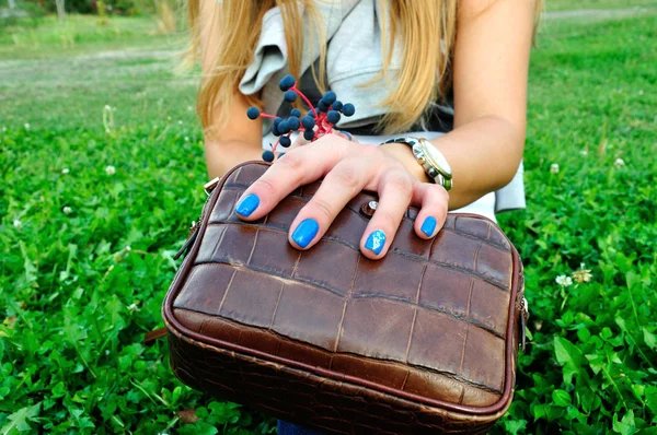 Woman fingers with blue manicure on clutch with green grass back — Stock Photo, Image