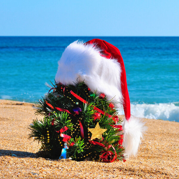 Christmas tree and santa hat on the sand in the beach