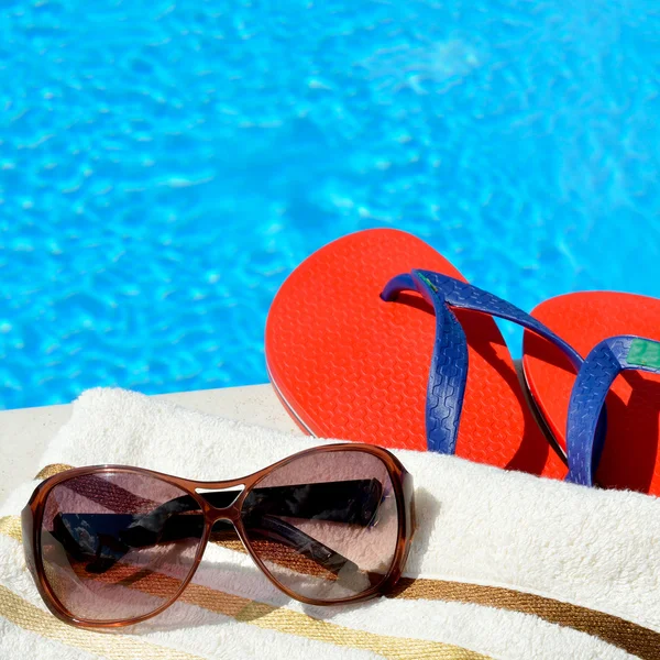 Zonnebril, strandhanddoek en slippers bij het zwembad. — Stockfoto