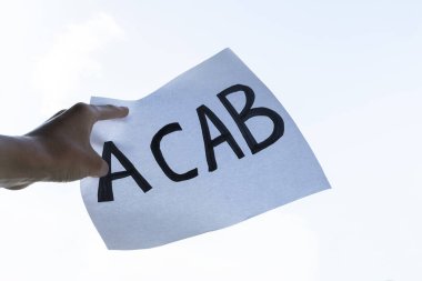 Erkek el üzerinde ACAB yazıları olan bir poster tutuyor. Gösteride ACAB işareti tutan protestocu, dikey görüntü